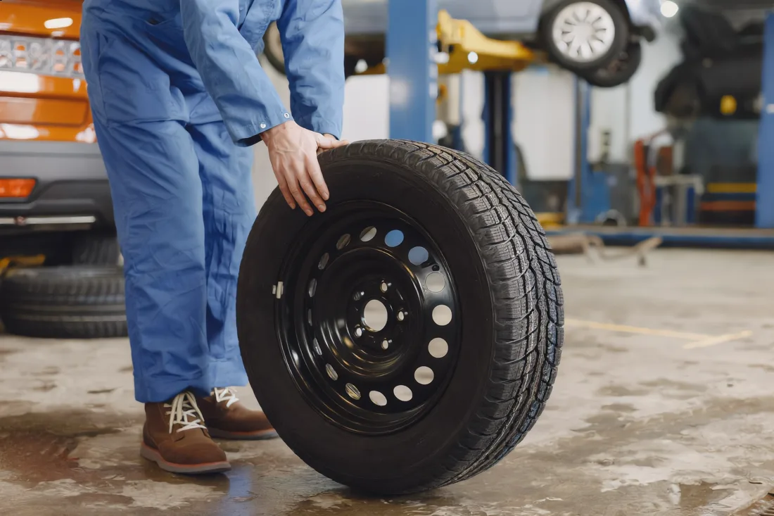 A mechanic rolling a new tire across the shop floor