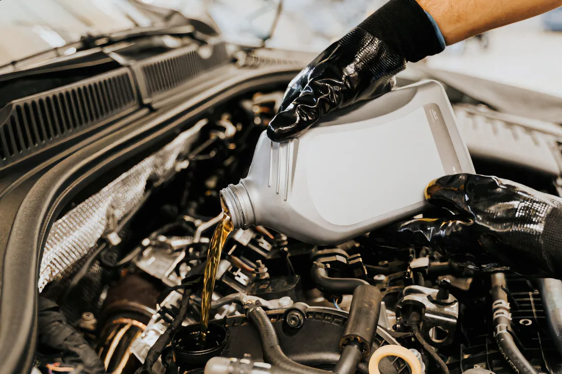 A mechanic pouring fresh motor oil into a car engine during an oil change